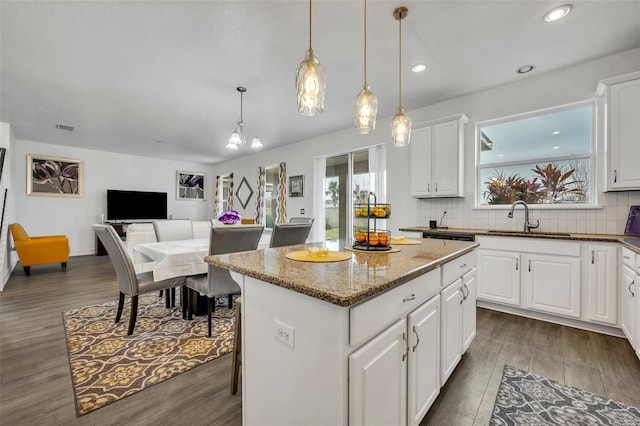 kitchen with sink, dark stone countertops, white cabinets, a kitchen island, and decorative light fixtures