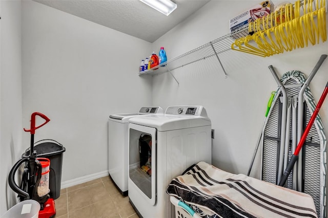 clothes washing area with a textured ceiling, washer and dryer, and light tile patterned floors