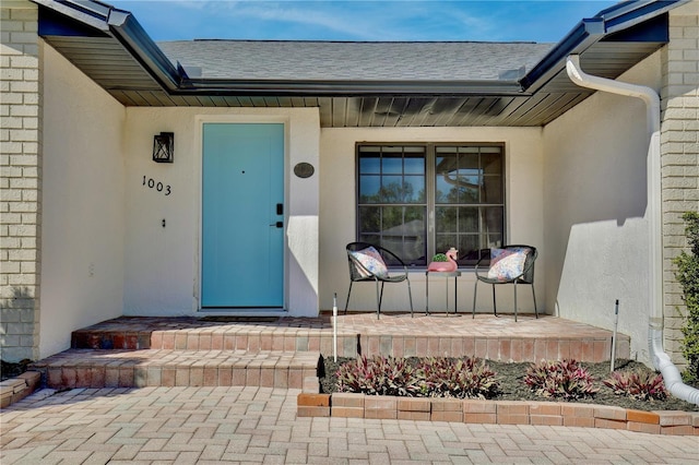 doorway to property featuring a shingled roof, brick siding, and stucco siding