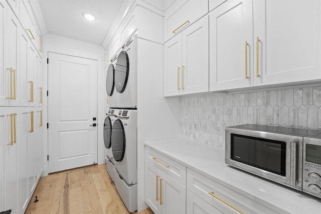 washroom featuring stacked washer / dryer, a textured ceiling, and light wood-type flooring