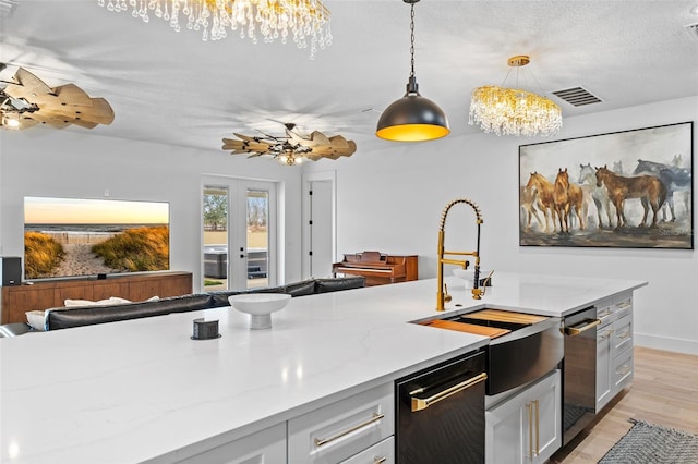 kitchen with pendant lighting, white cabinetry, light stone countertops, a textured ceiling, and french doors