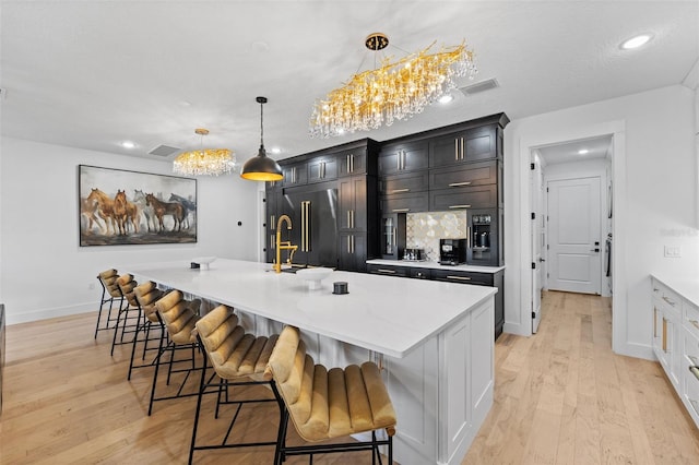 kitchen featuring built in fridge, a kitchen island with sink, a kitchen breakfast bar, and decorative light fixtures