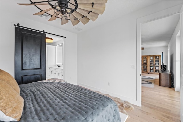 bedroom with connected bathroom, a barn door, and light wood-type flooring