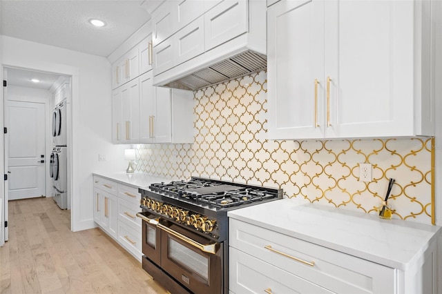14771 SE 60th St, Morriston, FL 32668 - kitchen with white cabinets, light wood-type flooring, custom exhaust hood, stacked washer and clothes dryer, and range with two ovens
