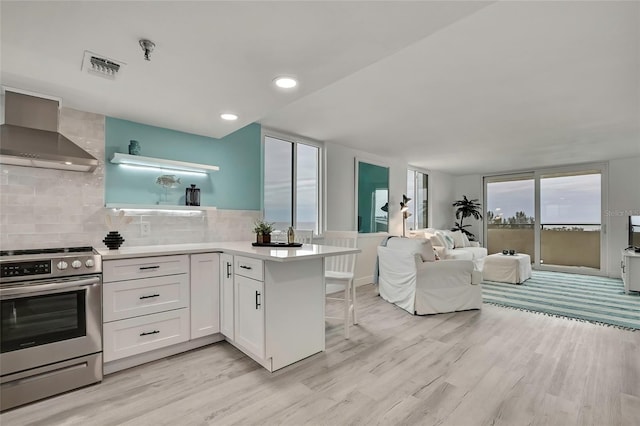 kitchen featuring stainless steel electric stove, tasteful backsplash, white cabinetry, kitchen peninsula, and wall chimney range hood