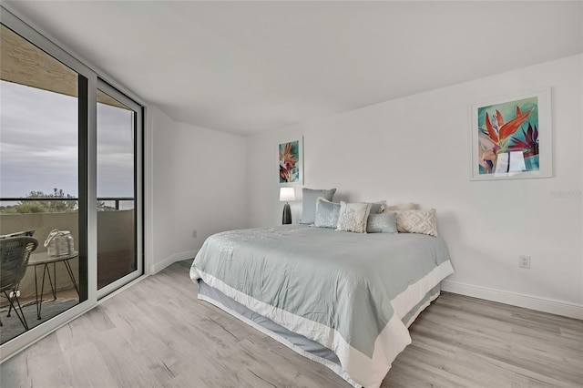 bedroom with access to exterior, expansive windows, and light wood-type flooring