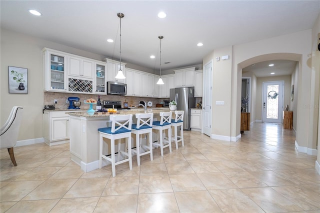 kitchen featuring appliances with stainless steel finishes, tasteful backsplash, white cabinets, a center island with sink, and decorative light fixtures