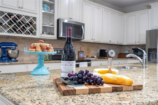 kitchen with sink, appliances with stainless steel finishes, light stone countertops, decorative backsplash, and white cabinets