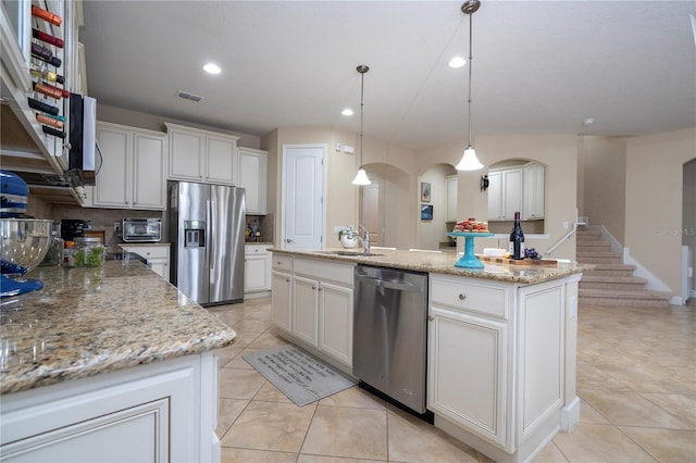 kitchen with appliances with stainless steel finishes, pendant lighting, white cabinetry, a kitchen island with sink, and light stone counters