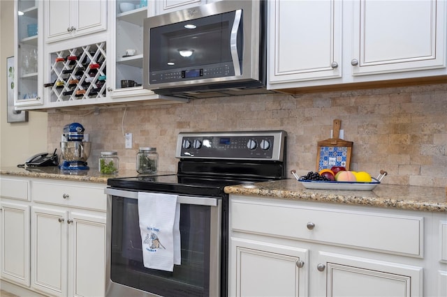 kitchen with white cabinetry, backsplash, light stone counters, and stainless steel appliances