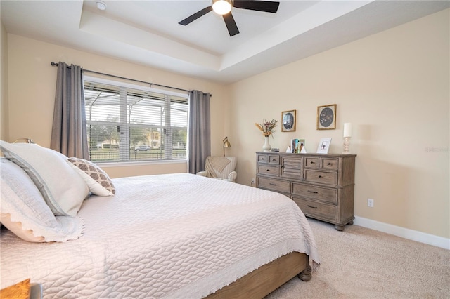 bedroom with a tray ceiling, light colored carpet, and ceiling fan