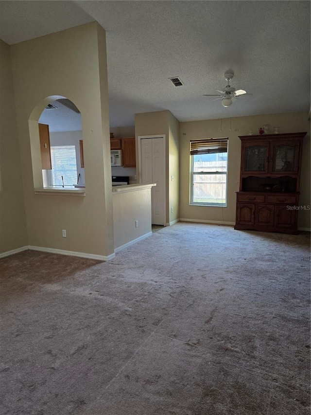 unfurnished living room featuring light carpet, a textured ceiling, and ceiling fan