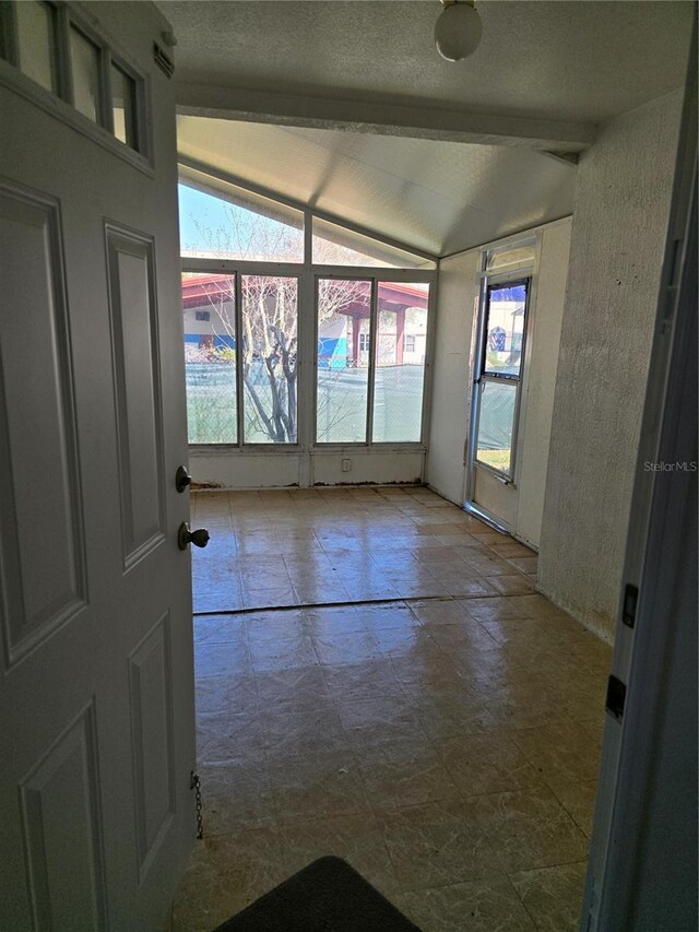 empty room featuring lofted ceiling with beams and a textured ceiling