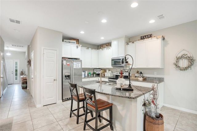 kitchen with light tile patterned flooring, dark stone countertops, a kitchen bar, a kitchen island with sink, and stainless steel appliances