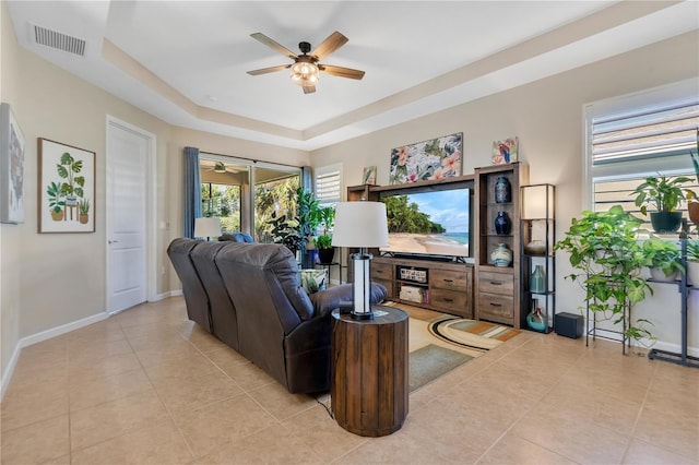 tiled living room featuring ceiling fan and a tray ceiling