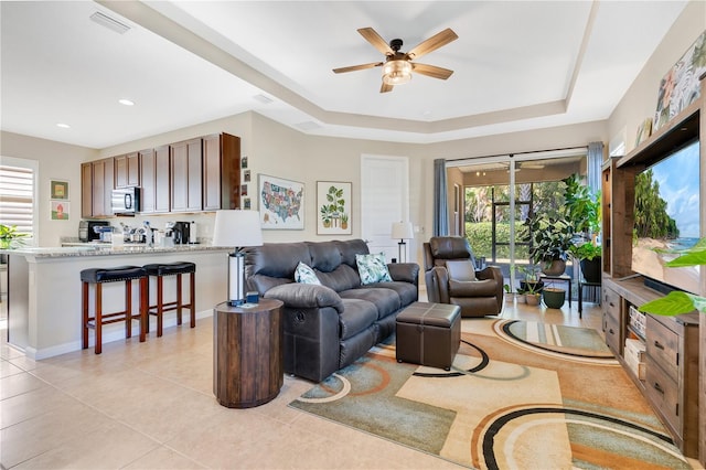 tiled living room featuring ceiling fan and a tray ceiling