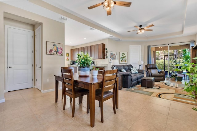 dining space with a raised ceiling, light tile patterned floors, and ceiling fan