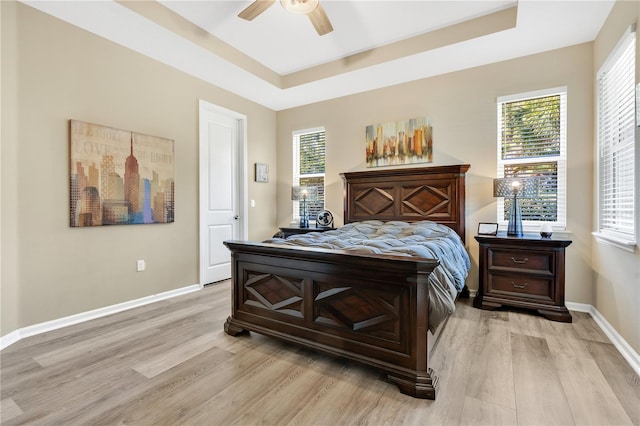 bedroom featuring multiple windows, a tray ceiling, light hardwood / wood-style flooring, and ceiling fan