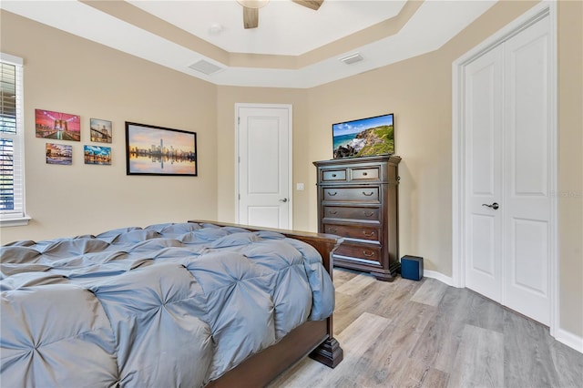 bedroom featuring a tray ceiling, light hardwood / wood-style floors, a closet, and ceiling fan