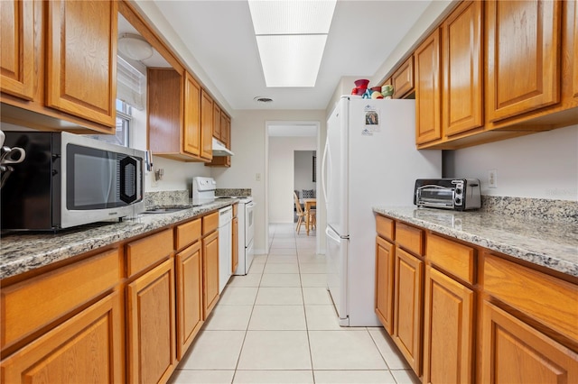 kitchen with white appliances, a skylight, light stone countertops, and light tile patterned flooring