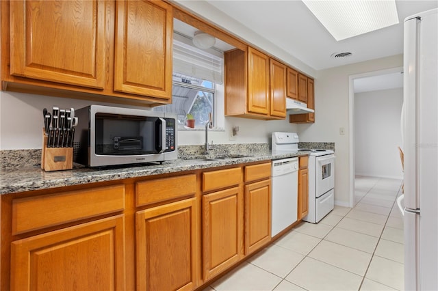 kitchen with sink, white appliances, light tile patterned floors, a skylight, and light stone counters