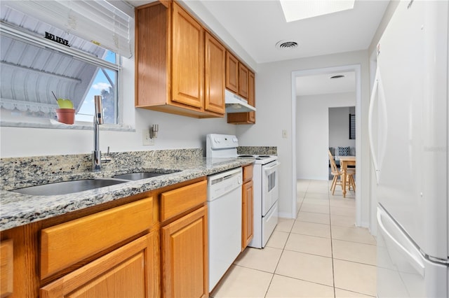 kitchen featuring light tile patterned flooring, a skylight, sink, light stone countertops, and white appliances