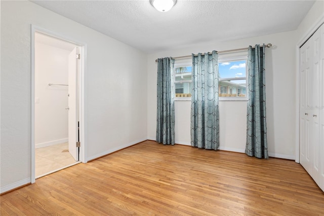 unfurnished bedroom with light hardwood / wood-style flooring, a closet, a textured ceiling, and ensuite bathroom