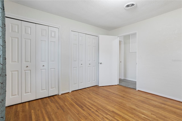 unfurnished bedroom featuring a textured ceiling, light hardwood / wood-style flooring, and multiple closets