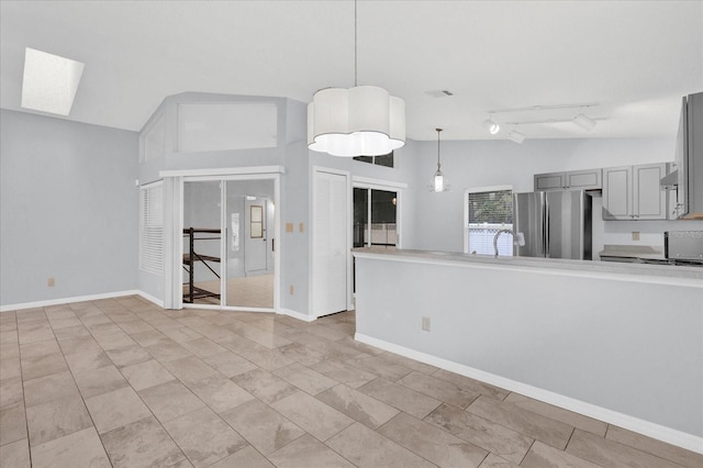 unfurnished living room with baseboards, visible vents, vaulted ceiling with skylight, a sink, and track lighting