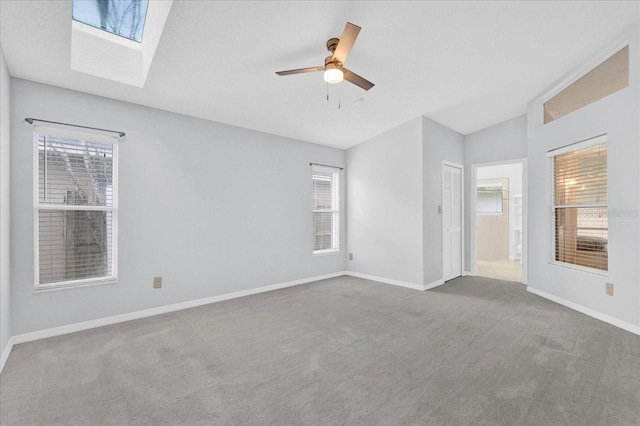 carpeted empty room featuring baseboards, ceiling fan, and vaulted ceiling with skylight