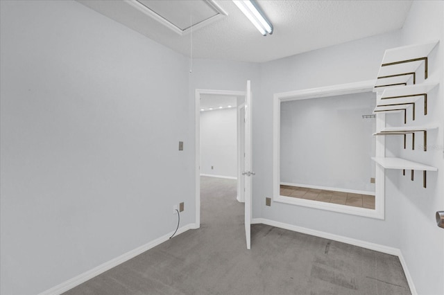 carpeted empty room with a textured ceiling, attic access, and baseboards