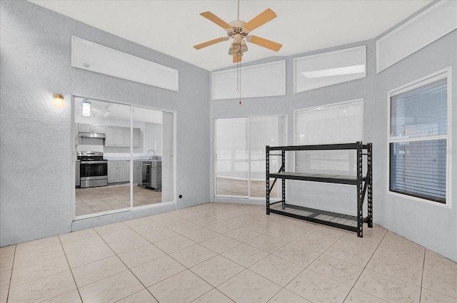 empty room featuring light tile patterned flooring, a textured wall, ceiling fan, and a sink