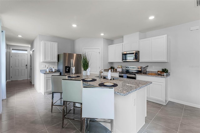 kitchen featuring stainless steel appliances, white cabinets, and a center island with sink