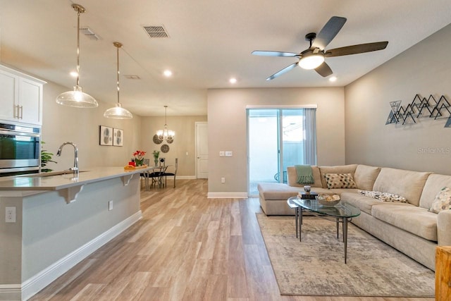 living room featuring ceiling fan with notable chandelier, sink, and light hardwood / wood-style flooring