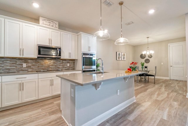 kitchen with stainless steel appliances, white cabinetry, hanging light fixtures, and a kitchen island with sink