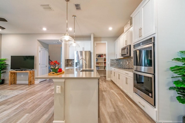 kitchen with white cabinets, pendant lighting, stainless steel appliances, light hardwood / wood-style floors, and backsplash