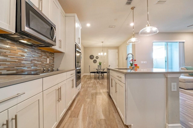 kitchen featuring sink, decorative light fixtures, a center island with sink, appliances with stainless steel finishes, and white cabinets