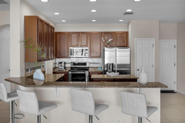 kitchen featuring appliances with stainless steel finishes, a breakfast bar, kitchen peninsula, and light tile patterned floors