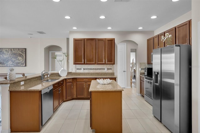 kitchen with sink, appliances with stainless steel finishes, a center island, light stone countertops, and kitchen peninsula