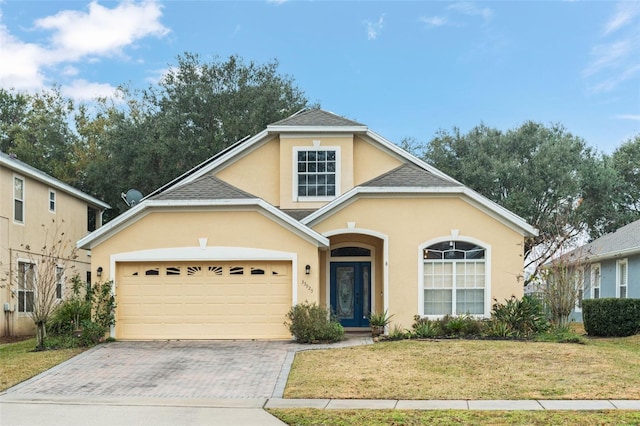 traditional home with a shingled roof, an attached garage, decorative driveway, a front lawn, and stucco siding