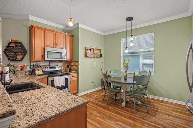 kitchen with light wood finished floors, appliances with stainless steel finishes, a sink, and ornamental molding