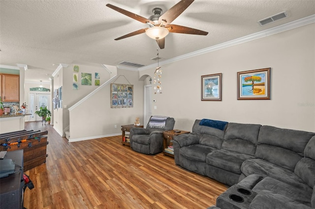 living area with arched walkways, visible vents, ornamental molding, wood finished floors, and stairs