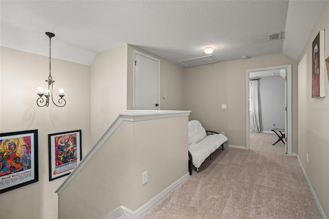 corridor with visible vents, light carpet, a textured ceiling, an upstairs landing, and baseboards