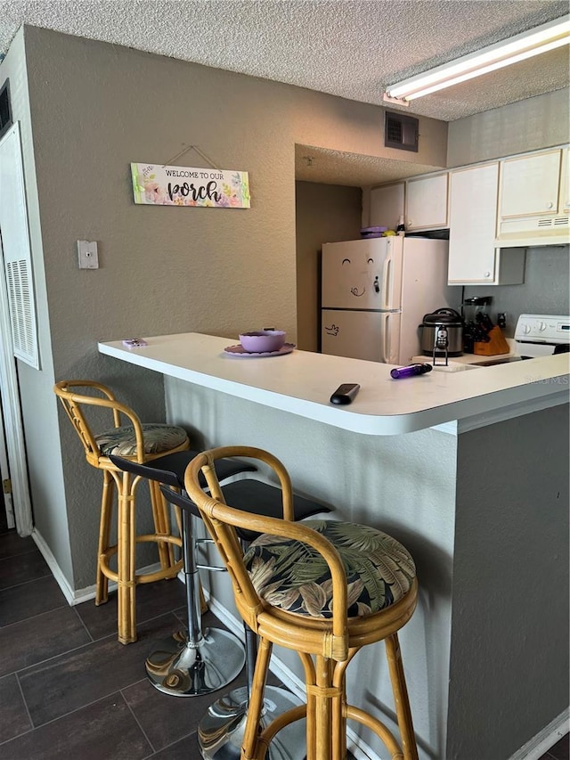 kitchen featuring white cabinetry, a breakfast bar area, white appliances, kitchen peninsula, and a textured ceiling