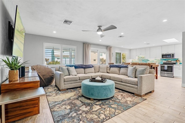 living room with ceiling fan, a skylight, and light wood-type flooring