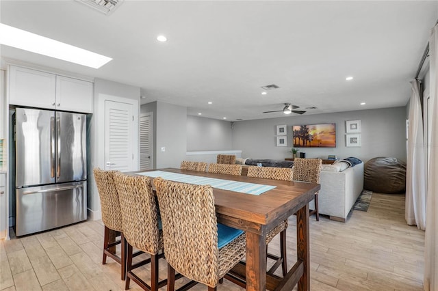 dining room featuring ceiling fan, a skylight, and light wood-type flooring