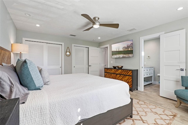 bedroom featuring connected bathroom, multiple closets, light hardwood / wood-style floors, and ceiling fan