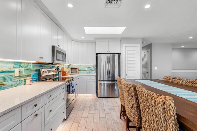 kitchen featuring backsplash, visible vents, a skylight, appliances with stainless steel finishes, and light wood-type flooring