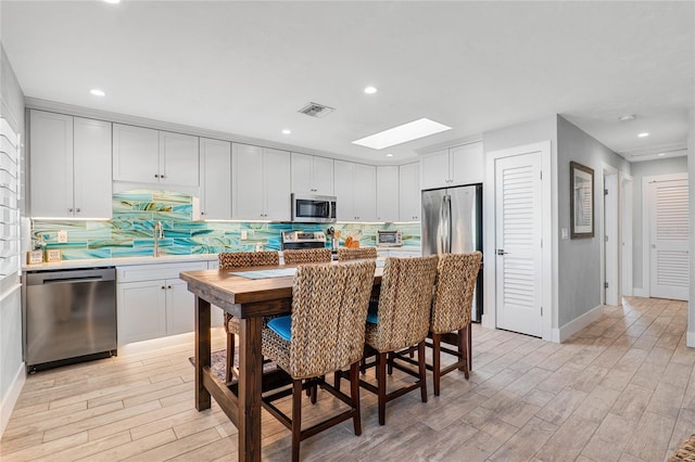 kitchen featuring light wood-type flooring, light countertops, appliances with stainless steel finishes, and a skylight