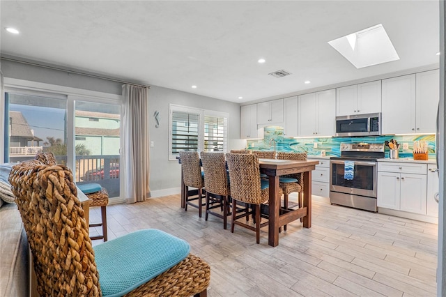 kitchen with appliances with stainless steel finishes, light wood finished floors, decorative backsplash, a skylight, and visible vents